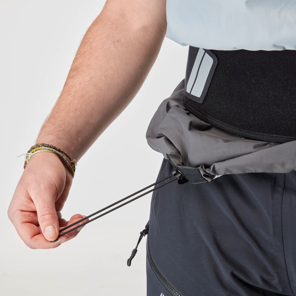 Wearing the NRS Stratos Short Sleeve Paddling Jacket, a person tightens a gray waterproof waist pack's drawstrings attached to a black belt, complementing their dark pants and light shirt.