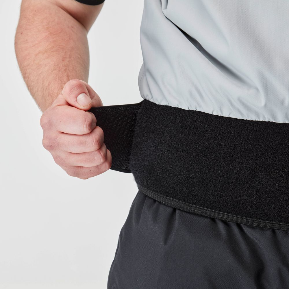 A person adjusts a black waist belt over dark pants and a light gray shirt, featuring neoprene seals for a snug fit, often seen in the NRS Stratos Short Sleeve Paddling Jacket designed with waterproof fabric for added protection.