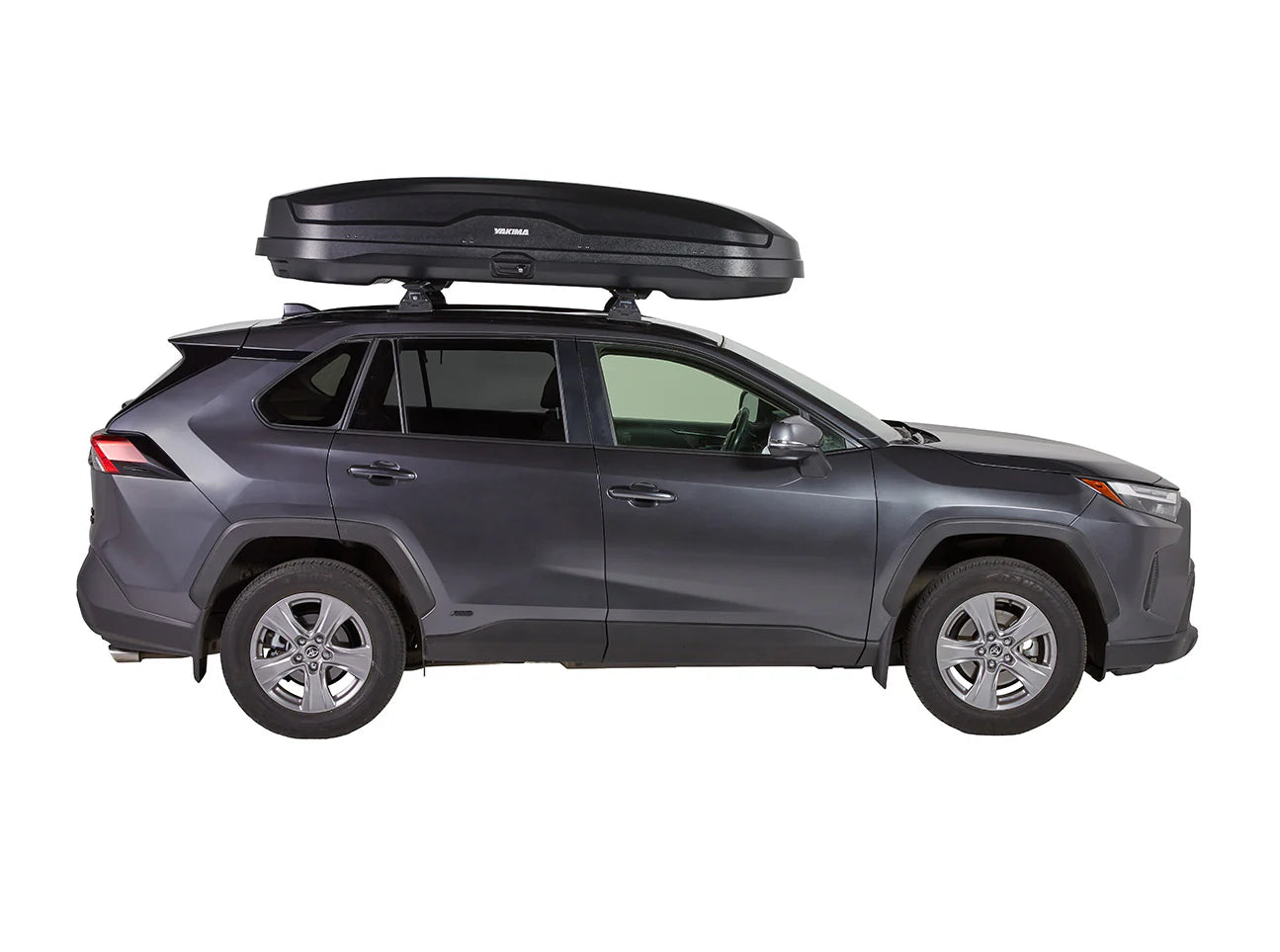 A dark gray SUV with a Yakima Skybox NX XXL, featuring the NX nano-texture finish, is seamlessly attached to its roof and parked side-on, ready for travel adventures.