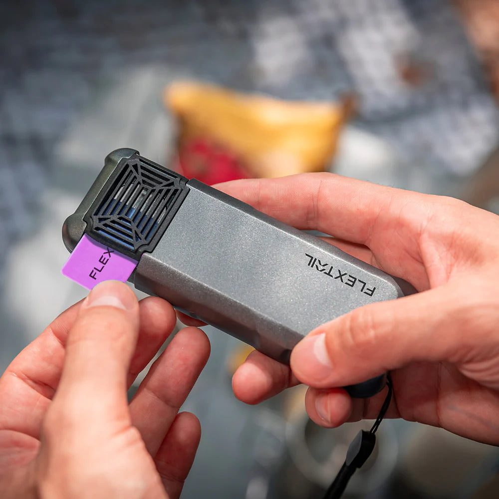 A person inserts a Flextail purple label into the Max Repeller Mosquito Repellent Device, which is equipped with a black vented cover and powered by a rechargeable 9600 mAh battery.