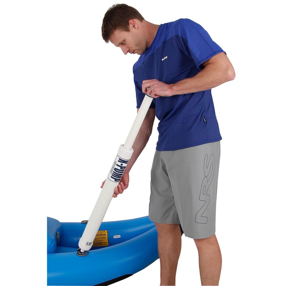 A man in a blue shirt and gray shorts uses the NRS K-Pump 200, known for its ergonomic design, to expertly inflate a blue object while ensuring the inflatable boat valves are perfectly sealed.