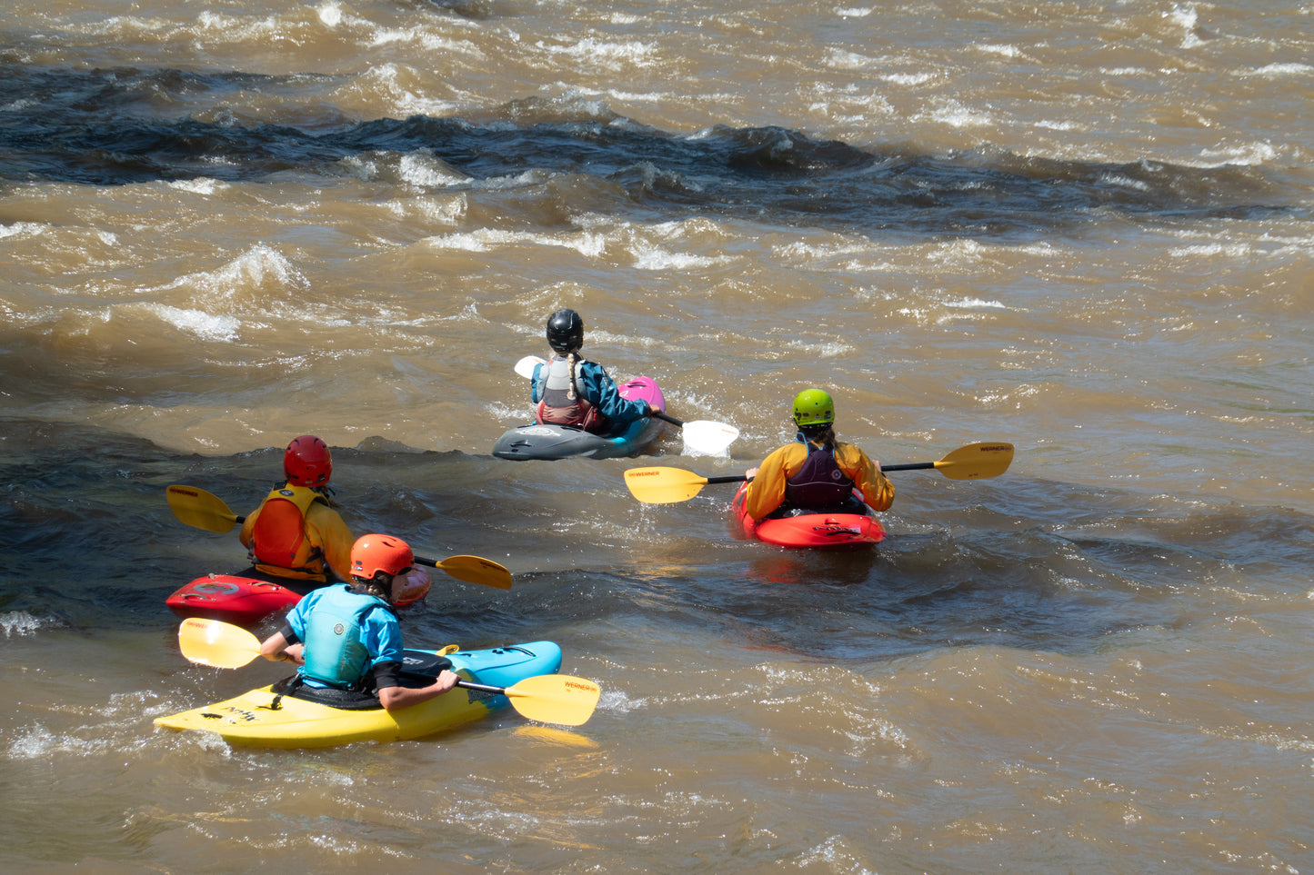 Four participants, equipped with 4CRS Paddle School's Adult Level 1 Kayak Class in the evenings, navigate the flowing river, showcasing their whitewater kayaking skills and emphasizing river safety.