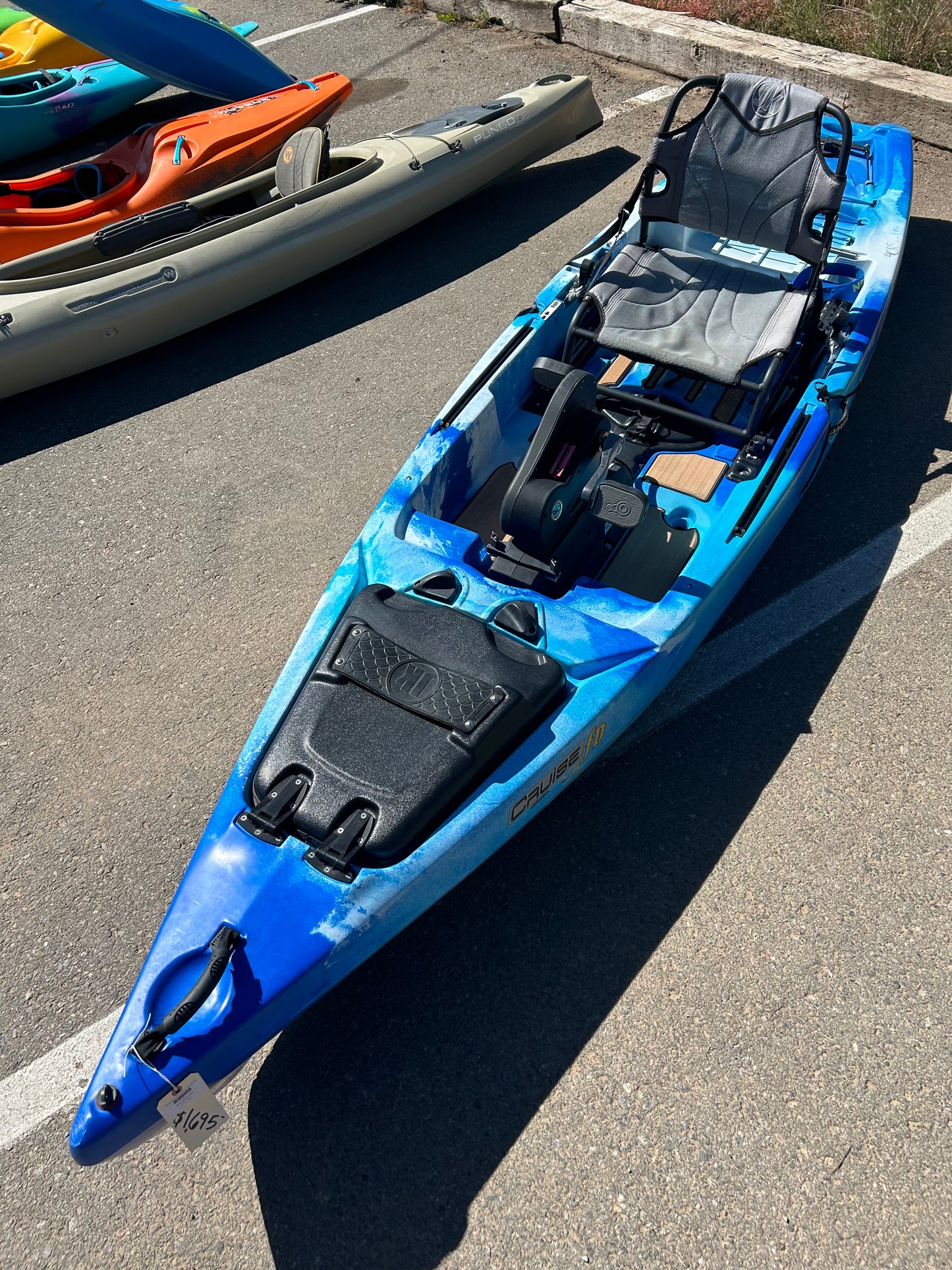 A Jackson Kayak Demo Cruise FD in blue and gray is parked on a paved surface, featuring a raised seat and storage compartments.