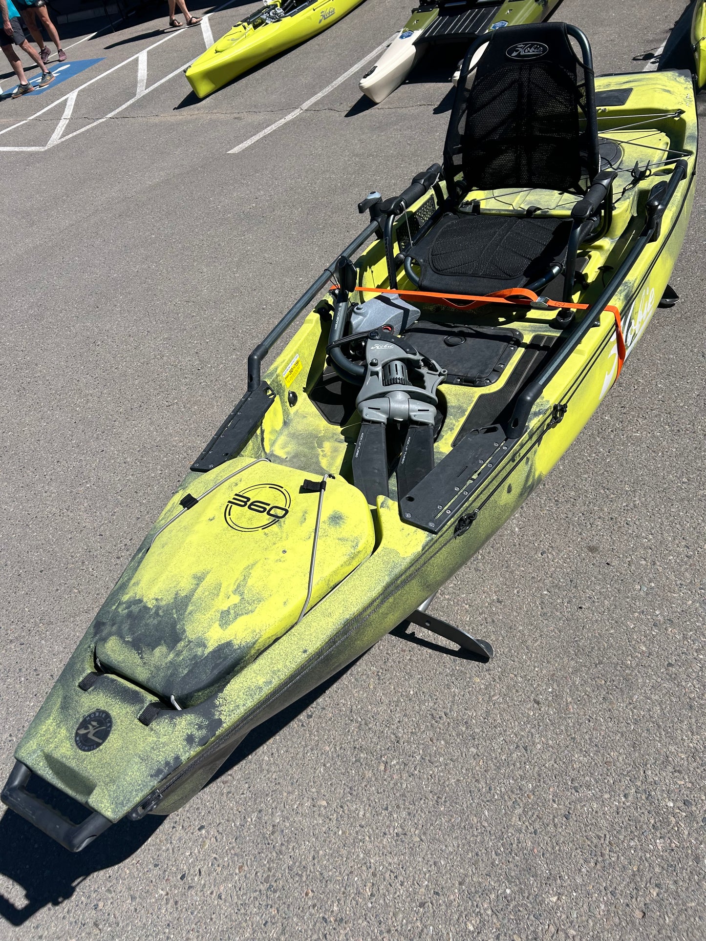 A lime green and black kayak is displayed outdoors, equipped with a black seat and foot pedals. This used Hobie Consignment 2021 Pro Angler 12 is an incredible find for fishing enthusiasts and comes with manageable shipping costs.