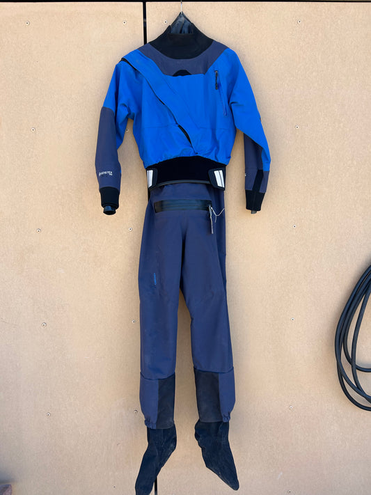 A blue and black Demo Drysuit - NRS Axiom Men's SM by NRS hangs on a wall. The suit appears unworn and in good condition, with attached socks at the ends of the legs.