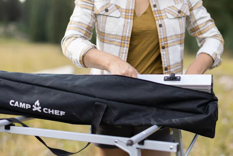 A woman holding a Camp Chef Mesa Adjustable Camp Table bag at an outdoor gathering.