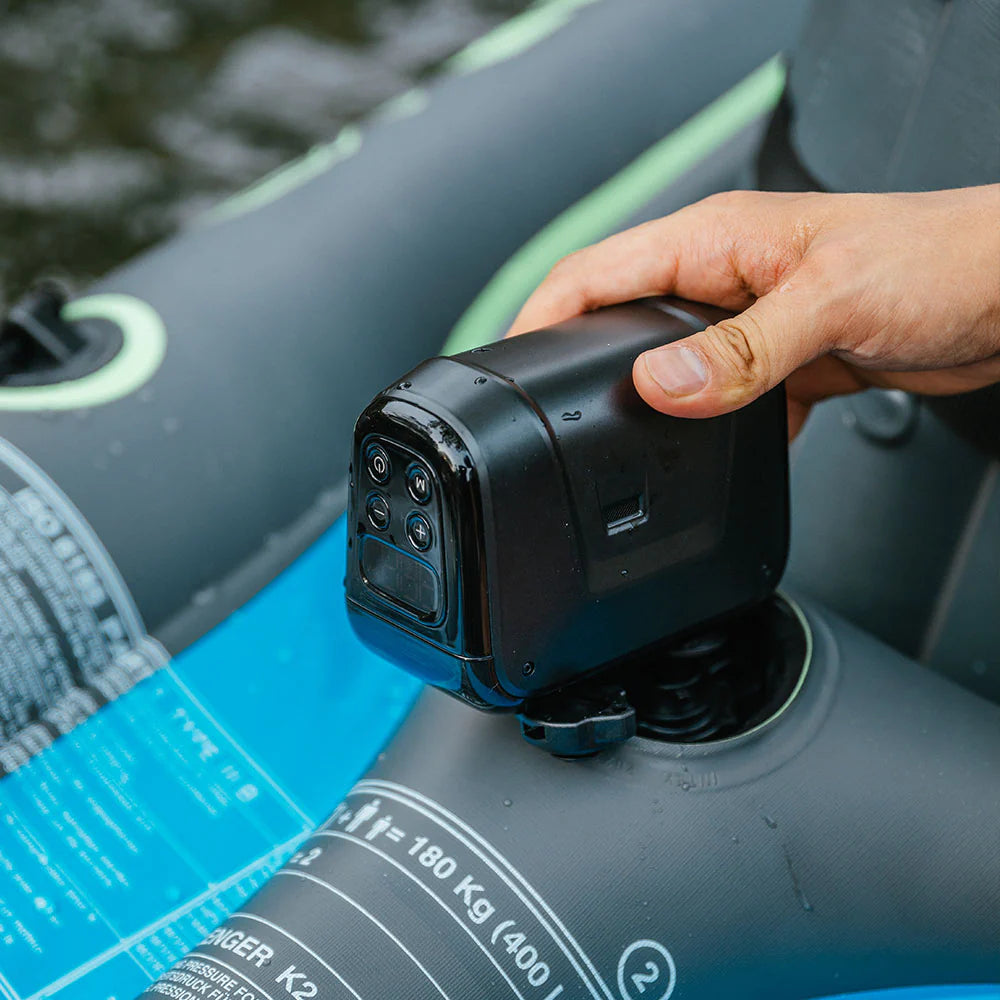 A hand is holding a black camera on an inflatable boat equipped with the MAX Electric Boat Pump by Flextail, gliding smoothly over the body of water.