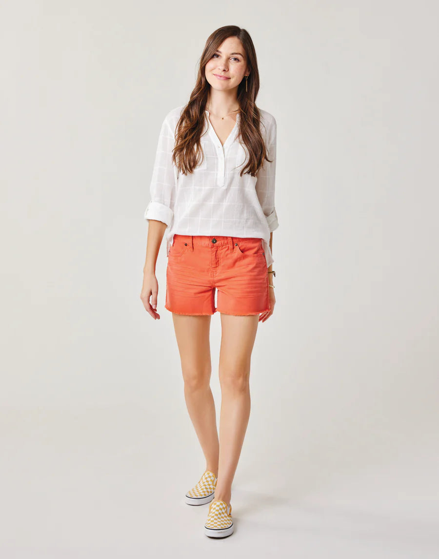 Someone with long hair wears a white shirt, Carve's orange Oahu 4" Stretch Cotton Corduroy Shorts, and yellow shoes against a plain background—a perfect addition to any vacation wardrobe.