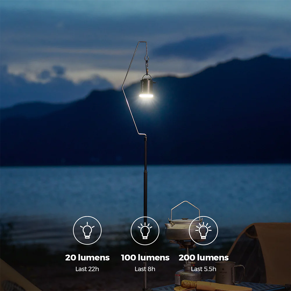 A campsite image displays a lantern on a stand adjacent to a table with cookware, with text below indicating light brightness levels: 20 lumens (22 hours), 100 lumens (8 hours), and 200 lumens (5.5 hours). Mountains are visible in the background, making it an ideal spot to use your Flextail Tiny Pump X for effortlessly inflating gear.