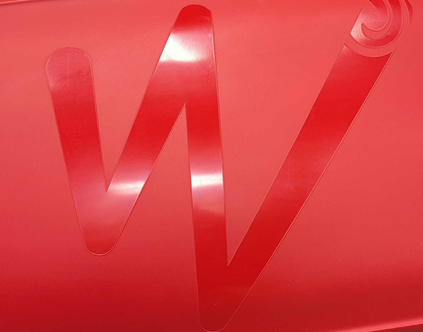 A large, stylized "W" from Waka Kayaks' Skuxx is embossed on a red surface, echoing the sleek form of a versatile boat gliding effortlessly through water.