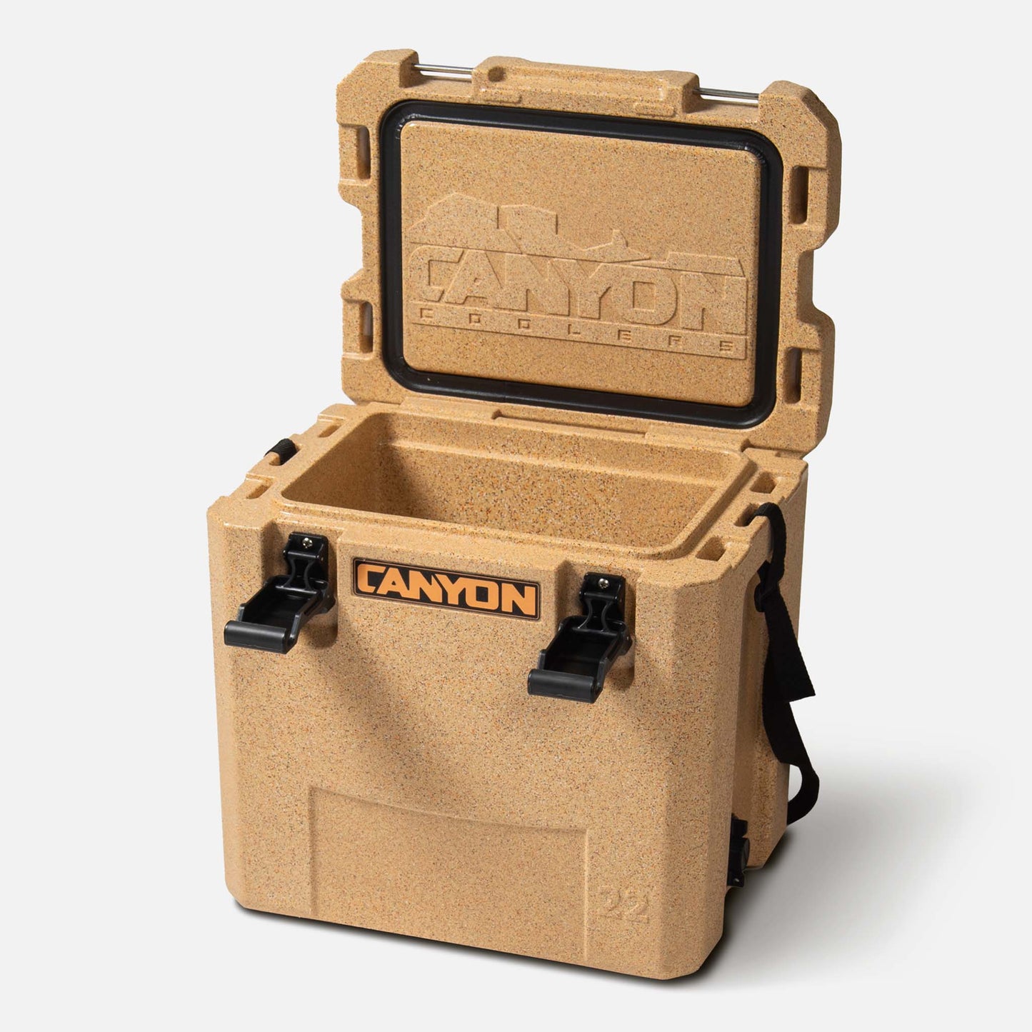 The tan Canyon Coolers Outfitter 22 V2 Cooler features an open lid with the embossed logo. Its rotomolded build and pressure-injected foam ensure durability. Two black latches and a carrying strap complete the design.