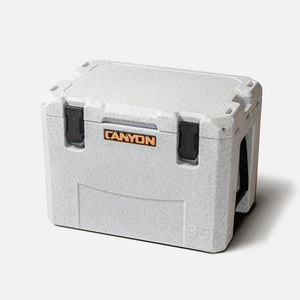 Introducing the Outfitter V2 Series Cooler by Canyon Coolers—a heavy-duty, gray cooler with a textured exterior. It features the iconic "Canyon" logo on the front, sturdy latches, reinforced corners, and is crafted from premium sun-resistant polymer.