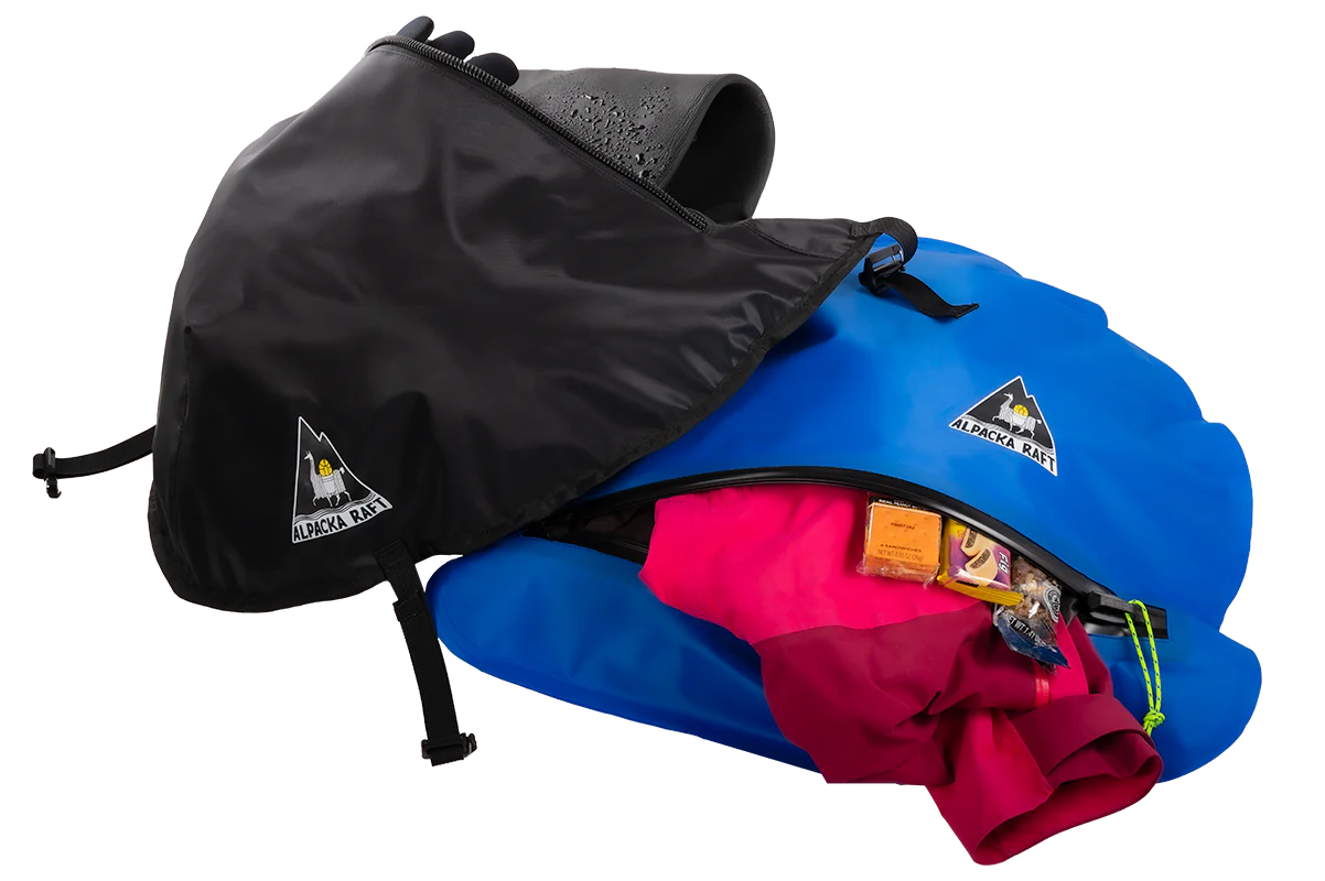 A blue and black Alpacka packraft with a partially open Hybrid Bow Bag zipper, revealing pink fabric and gear inside, perfect for wet storage.