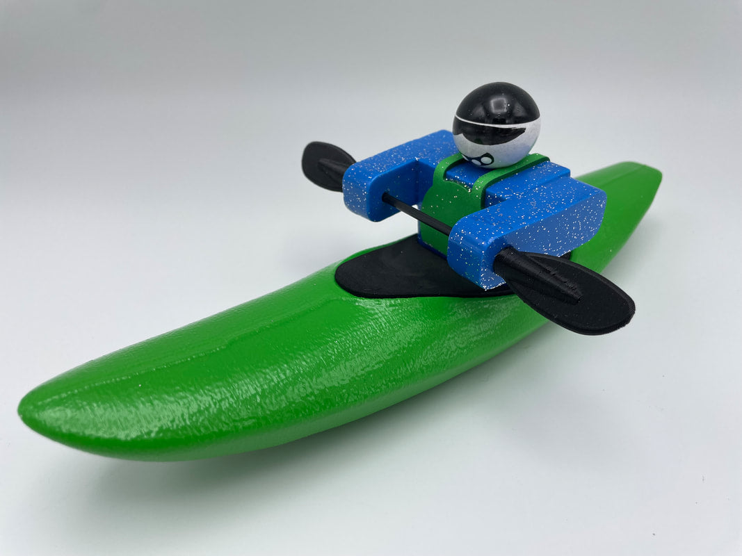 A Foamie Creeker from the Foamie Friends collection, complete with a helmet, navigates a green kayak on a plain background, poised for river adventures.