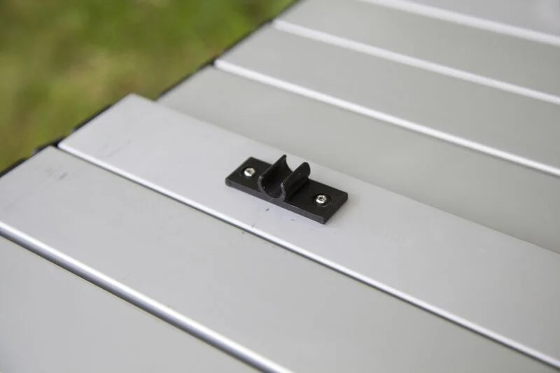 A black metal bracket on a white Camp Chef Mesa Adjustable Camp Table for an outdoor gathering.