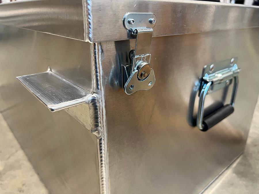 The Down River Equipment Gunnison Drybox, crafted from aircraft-grade aluminum, features a shiny surface with secure latch and handle. Visible weld lines highlight the corners, while the handle includes a comfortable black grip. A rubber gasket ensures outstanding durability and protection.