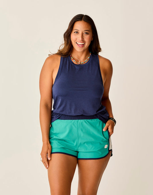 A person smiling while wearing a Carve Tide Tank and green shorts against a neutral background.