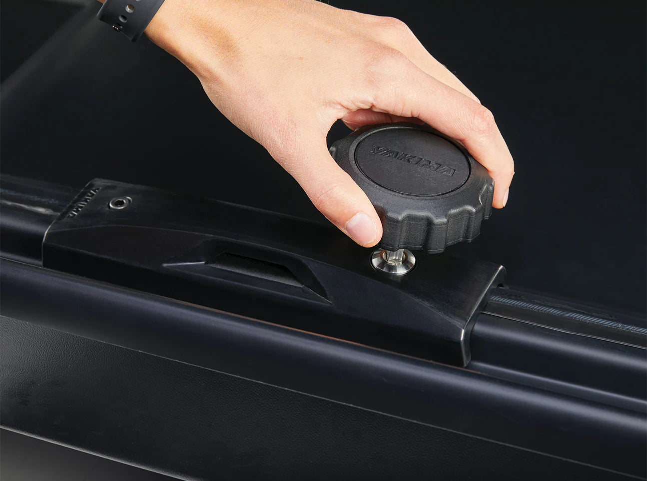 Gently hand tighten the large circular knob on the black rectangular element of the Yakima Skybox NX XXL to securely pack your travel gear in this sleek cargo box.