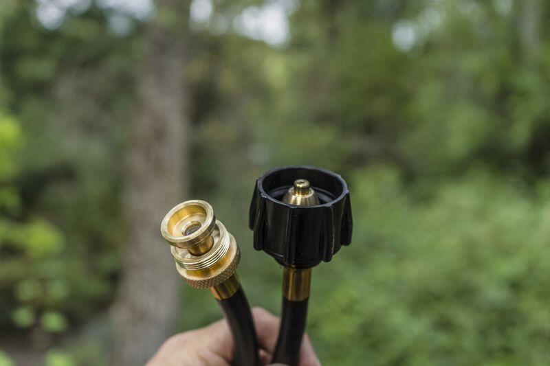 A Camp Chef Propane Tank Adapter Hose standing in front of a wooded area.