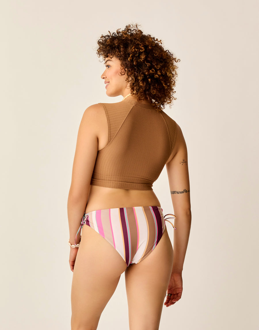 A person with curly hair models the Ibiza Reversible Bottom by Carve, wearing it with a brown sleeveless top, viewed from the back against a plain background.