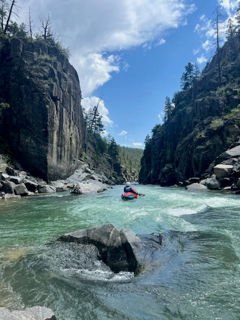 Paddling through a narrow, rocky canyon on a clear day, with trees lining the cliffs, feels like an adventure straight out of the ACA Packraft Instructor Certification by 4CRS Paddle School.