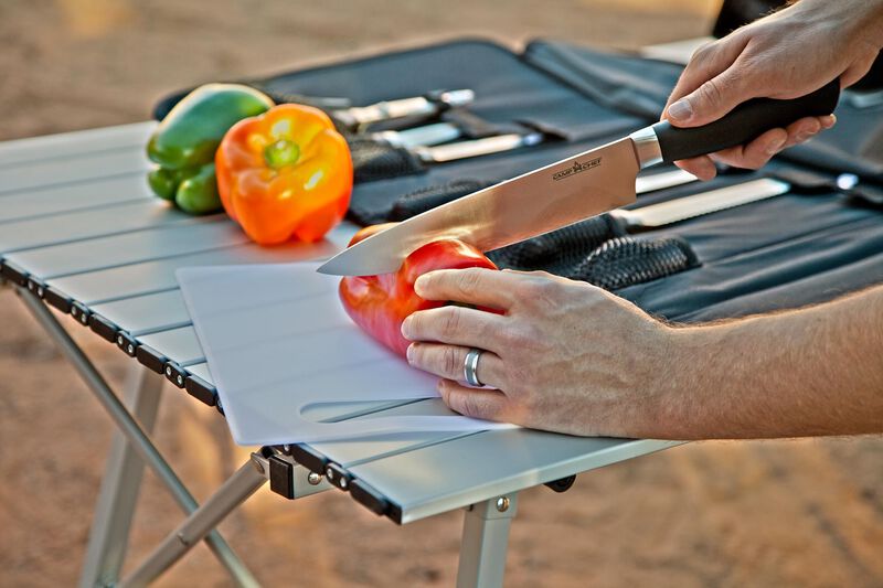 A chef cutting vegetables on a table with a Camp Chef Professional 9 piece Knife Set.