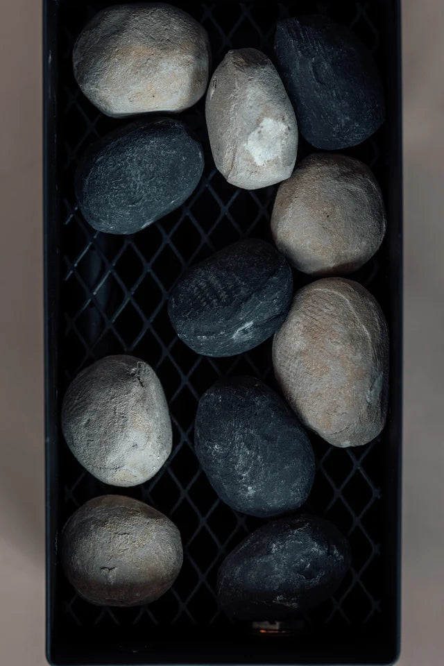 The Original LavaBox Combo by LavaBox features a black rectangular tray that resembles a sleek portable firepit, holding eleven smooth stones—some grey and others dark—arranged on a grid-like surface.