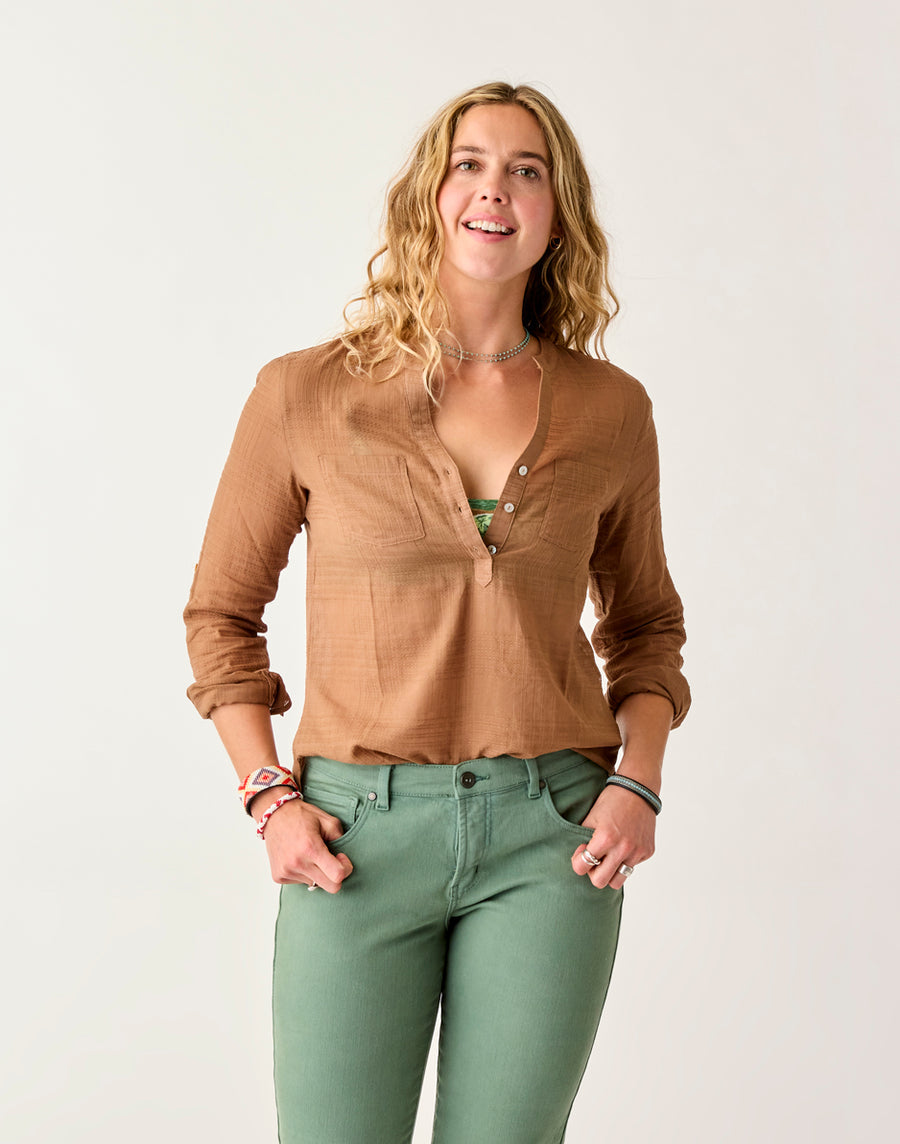 A person with long hair is smiling against a plain background, wearing a Dylan Textured Shirt by Carve and green pants.