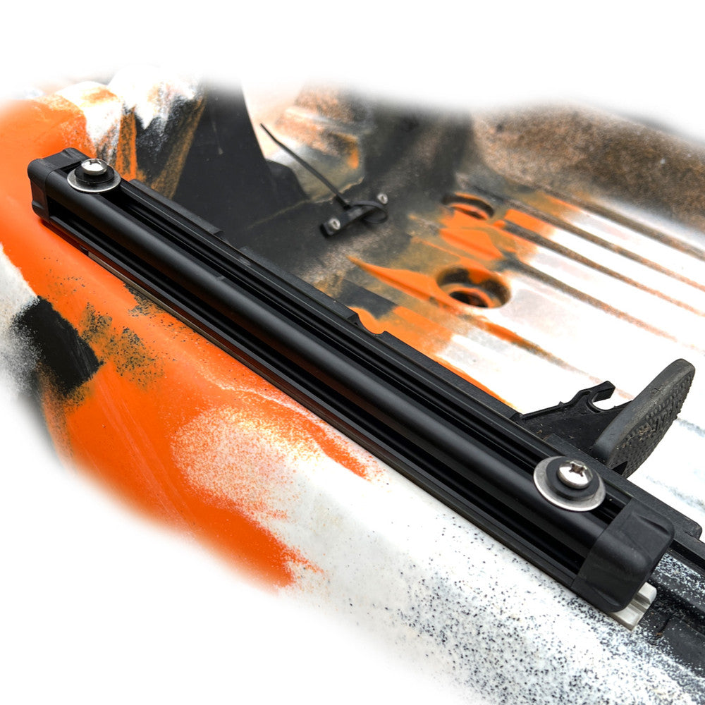 A close-up of the Jackson Kayak TriTrak Kit mounted on a surface with black, orange, and white paint. The rail is secured by bolts on both ends, showcasing the precision of Jackson Kayak technology for versatile fishing mounting options.